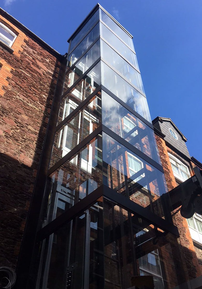Estructura de ascensor exterior en cristal junto a edificio de ladrillo